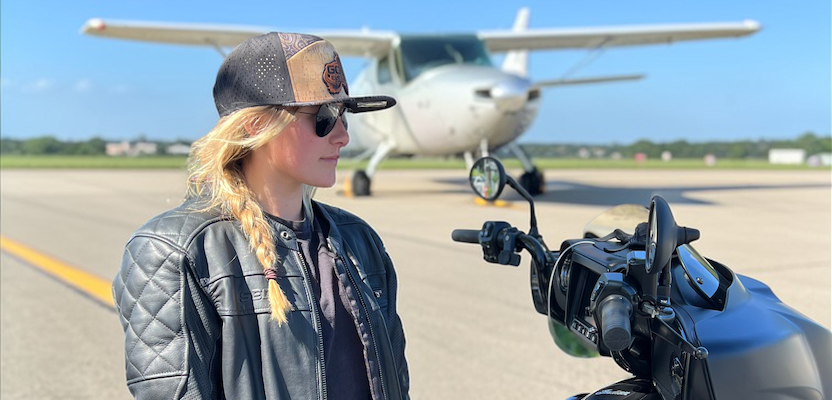 Woman wearing a custom hat with a motorcycle on an airport tarmac with a small airplane in the background