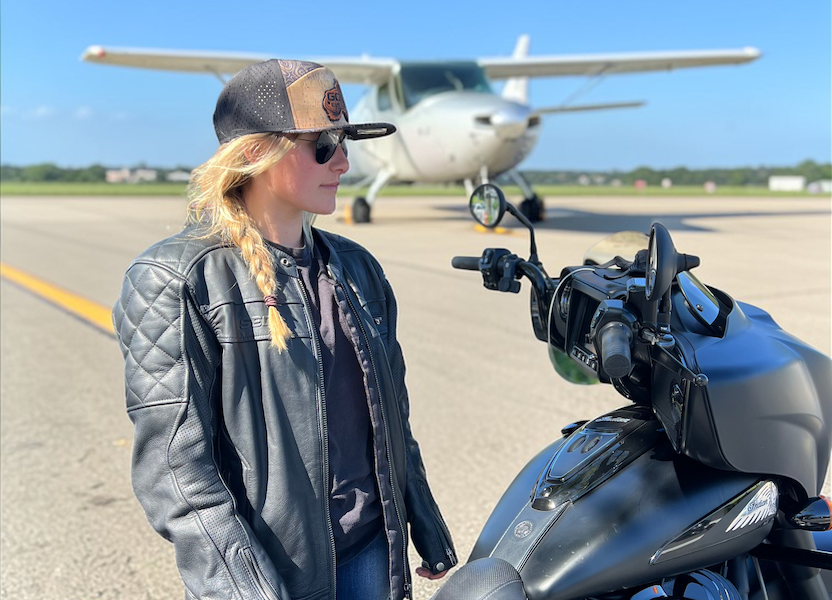 Woman wearing a custom hat with a motorcycle on an airport tarmac with a small airplane in the background