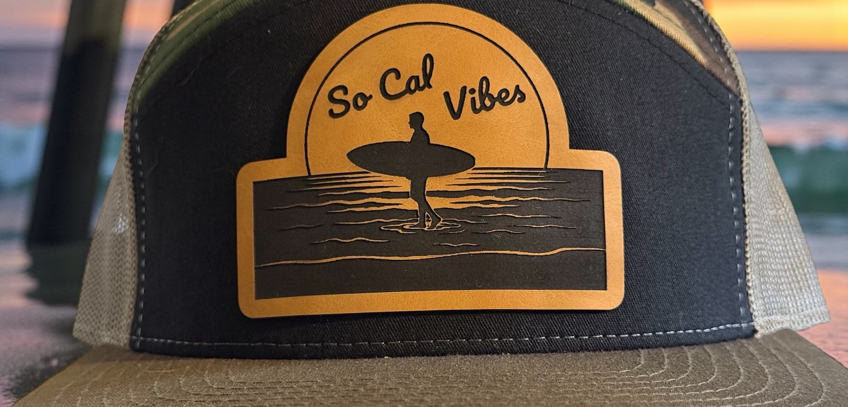 Custom trucker hat with 'So Cal Vibes' design featuring a surfer silhouette against a sunset, with a beach background
